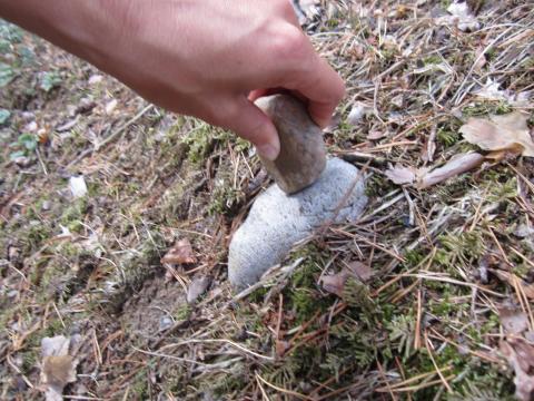 Eine Hand, die einen Stein hält und diesen auf einen am Boden liegenden Stein schlägt